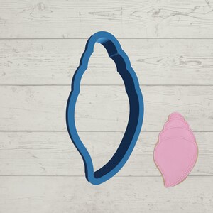 May include: A blue plastic seashell cookie cutter with a pink seashell cookie next to it.