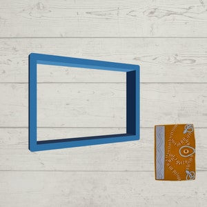 May include: A blue picture frame with a brown leather-bound journal with a stitched eye and other decorative stitching. The journal is on a white wood background.