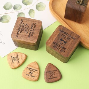 Peut inclure: Boîtes à souvenirs et médiators en bois avec texte gravé. Les boîtes sont carrées et les médiators en forme de goutte d'eau. Le texte indique "IN MEMORY OF JANE 1938-2022 GRACE & DANIEL JULY 22, 2024" avec des graphiques de cœur et de lunettes de soleil.