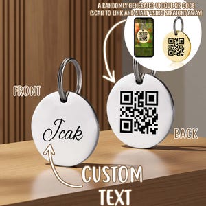 May include: A circular silver-toned metal tag featuring a split ring. The front side displays the custom text "Icak" in a black script font. The back side features a black printed QR code. A small inset shows a smartphone scanning the QR code.