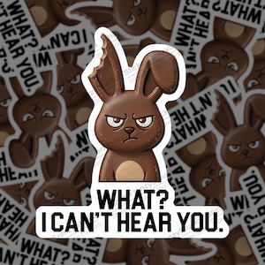 May include: A brown sticker featuring an angry cartoon bunny with a bite taken out of its ear. The sticker has the text "WHAT? I CAN'T HEAR YOU." in bold, white letters. The background shows similar stickers.