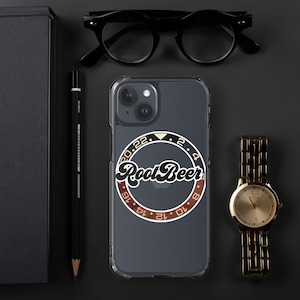 Pode incluir: Uma capa transparente para telefone com um design preto e dourado. O design apresenta um círculo com o texto "Root Beer" em uma fonte de letra preta. O círculo é rodeado por um anel dourado com os números 20, 22, 2, 4, 6, 8, 10, 12, 14, 16, 18 e 20.