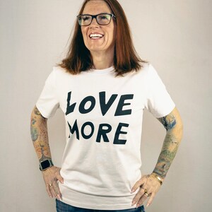 May include: White t-shirt with black text that reads "LOVE MORE".