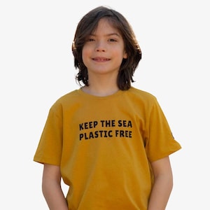 May include: A young person wearing a mustard yellow t-shirt with the text "KEEP THE SEA PLASTIC FREE" printed in black.