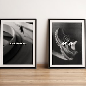 May include: Two framed black and white photographs. The left photo shows a person running on a curved path with the word "SALOMON" printed below. The right photo shows a close-up of a black and white running shoe with a white logo.