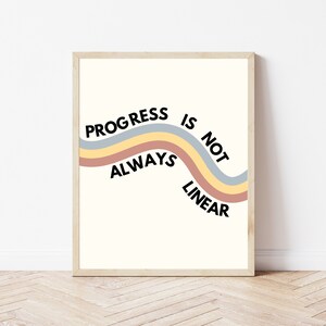 May include: A framed print with a white background and a colorful wavy line with the text "Progress is not always linear" in black.
