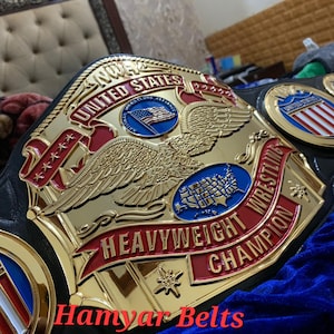 Könnte beinhalten: Ein gold-roter NWA United States Heavyweight Wrestling Champion Gürtel. Der Gürtel zeigt einen Adler, eine Karte der Vereinigten Staaten und den Text "Heavyweight Champion". Der Text "Hamyar Belts" ist ebenfalls sichtbar.