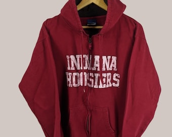 Może przedstawiać: Czerwona bluza z kapturem zapinana na zamek błyskawiczny z nadrukiem "Indiana Hoosiers" w kolorze białym na przodzie.