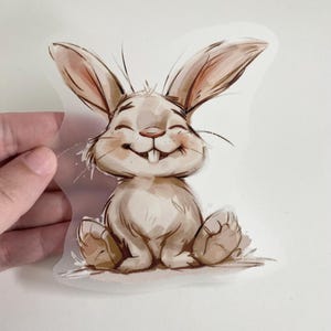 Puede incluir: Una ilustración de dibujos animados de un conejo marrón con orejas grandes y una amplia sonrisa. El conejo está sentado sobre sus patas traseras con sus patas delanteras metidas. El fondo es gris claro.