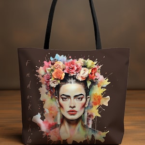 May include: A brown tote bag with a colorful watercolor illustration of Frida Kahlo with a flower crown. The text "Frida Kahlo" is written vertically on the left side of the bag.