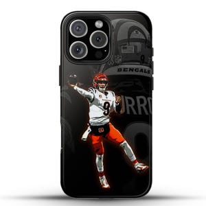 Puede incluir: Carcasa negra para iPhone con un gráfico de un jugador de fútbol americano con una camiseta blanca con rayas naranja y negras, lanzando un balón de fútbol. El número del jugador es 9. El texto "Bengals" y "Burrow" es visible en la carcasa.