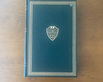 May include: A dark green hardcover book with a gold border and a gold embossed Harvard University seal with the words "VERI TAS".