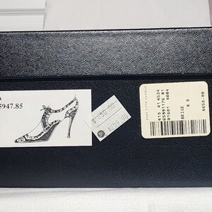 K&ouml;nnte beinhalten: Ein schwarzer Schuhkarton mit einem wei&szlig;en Etikett, auf dem "95A A05947.85" steht und eine Zeichnung eines schwarz-wei&szlig;en High-Heel-Schuhs. Es gibt ein Preisschild mit der Aufschrift "259,90 &euro;" und ein wei&szlig;es Etikett mit Barcode und Text, auf dem "SAKS FIFTH AVENUE 415 41 4534 65991176 81 01601 4084 BEIGE 8 650,00 &euro;" steht.