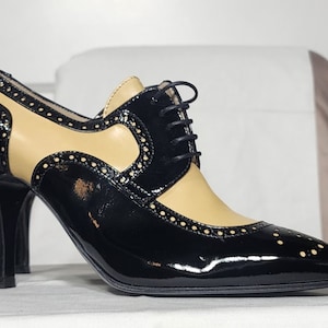 K&ouml;nnte beinhalten: Schwarze und braune Lederschuhe mit Absatz, Schn&uuml;rung vorne und Brogue-Muster.