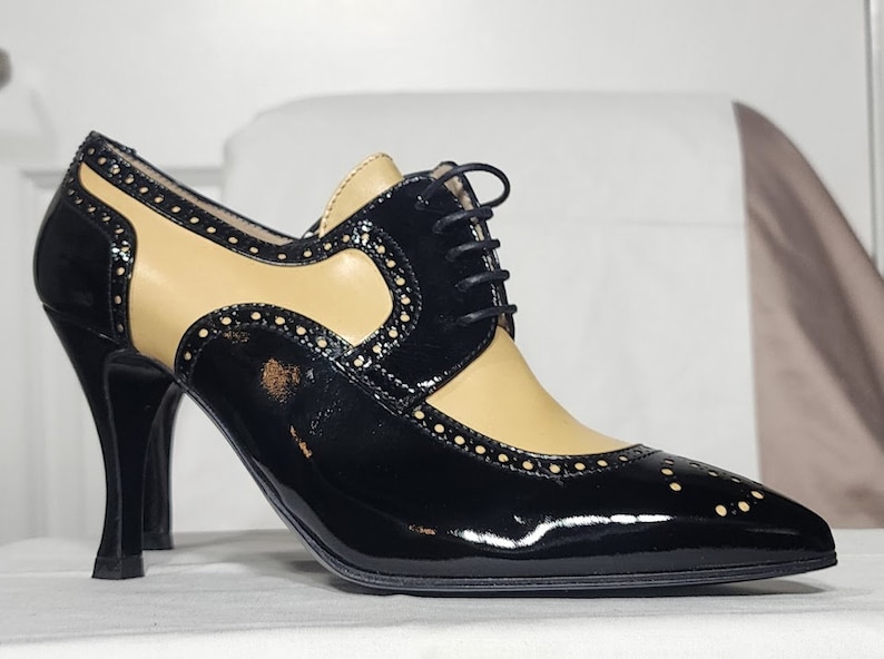 K&ouml;nnte beinhalten: Schwarze und braune Lederschuhe mit Absatz, Schn&uuml;rung vorne und Brogue-Muster.