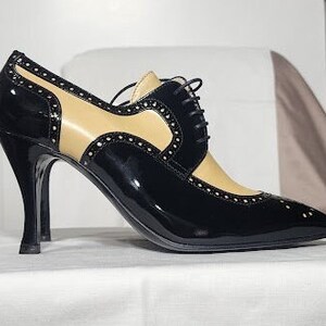 K&ouml;nnte beinhalten: Schwarze und braune Lederschuhe mit Absatz, Schn&uuml;rung vorne und spitzer Zehenpartie.