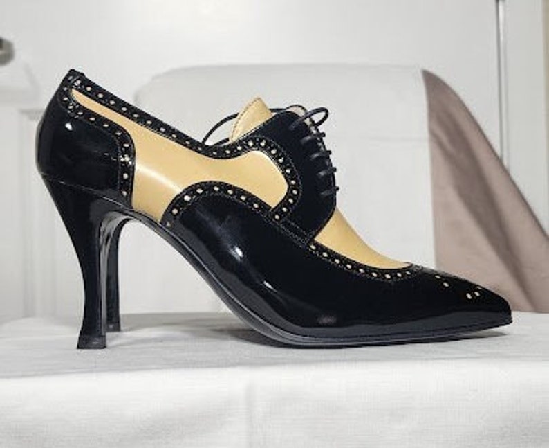 K&ouml;nnte beinhalten: Schwarze und braune Lederschuhe mit Absatz, Schn&uuml;rung vorne und spitzer Zehenpartie.