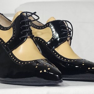 K&ouml;nnte beinhalten: Ein Paar schwarze und braune Lederschuhe mit Absatz, Schn&uuml;rung und Brogue-Muster.