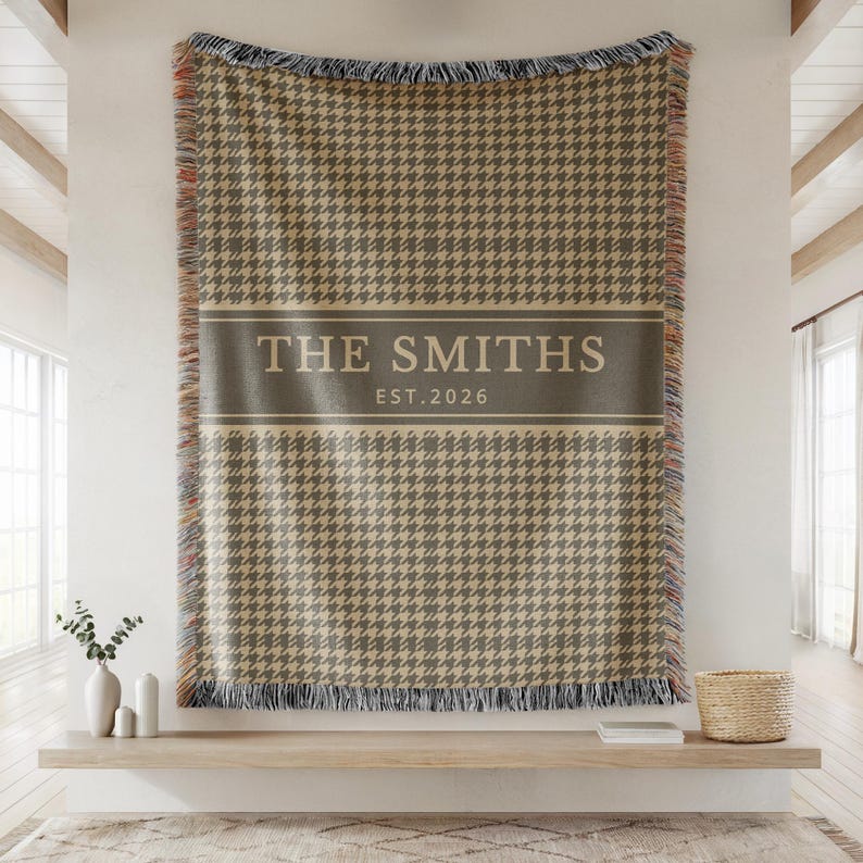 May include: A woven throw blanket featuring a brown and beige houndstooth pattern with a solid horizontal band across the center. The band displays the text THE SMITHS and EST. 2026 in a light-colored font. The blanket has fringed edges.