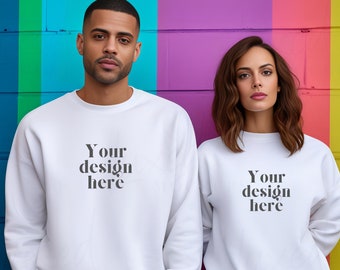 May include: Two white sweatshirts with the text "Your design here" printed on the front. The sweatshirts are being modeled by two people standing in front of a colorful wall.