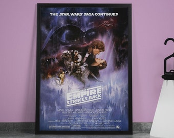 May include: A framed movie poster for the film "Star Wars: The Empire Strikes Back". The poster features a dark background with a scene from the movie, including Darth Vader, Luke Skywalker, Princess Leia, and Han Solo. The title of the film is in large, white letters at the bottom of the poster.