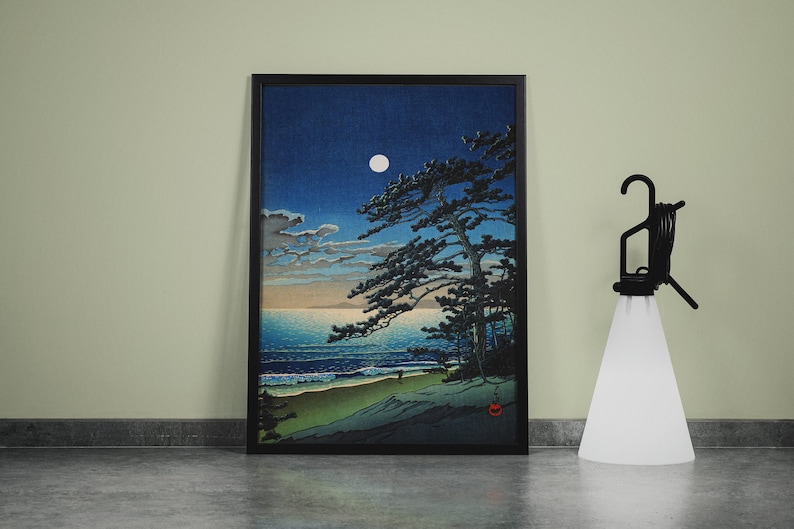 Puede incluir: Impresi&oacute;n art&iacute;stica enmarcada que representa una escena costera iluminada por la luna con un gran pino. La obra presenta un cielo azul oscuro, una luna llena y una playa con suaves olas. A la derecha hay una l&aacute;mpara negra con una pantalla blanca.