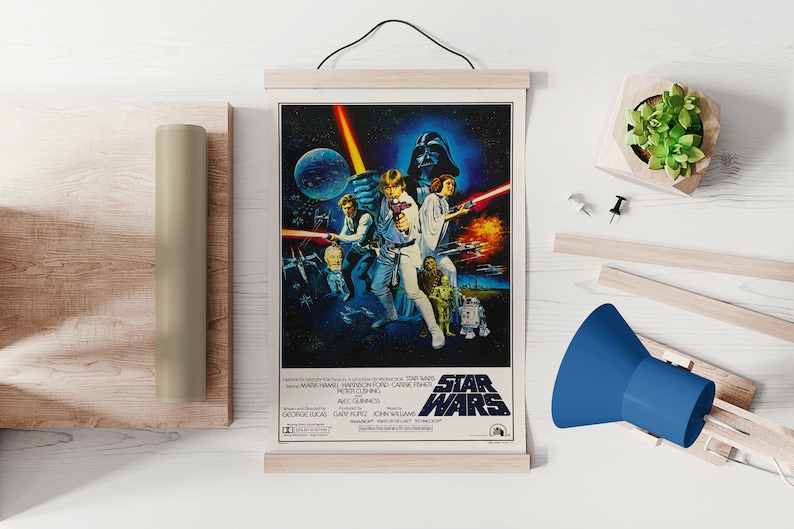 Może przedstawiać: Winietyczny plakat filmu Gwiezdne Wojny przedstawiający grupę postaci z filmu, w tym Luke'a Skywalkera, Hana Solo, księżniczkę Leię, Chewbakkę i Dartha Vadera. Plakat umieszczony jest na ciemnoniebieskim tle z gwiazdami i planetami. Tytuł "Gwiezdne Wojny" wyświetlany jest ż&oacute;łtymi literami na dole plakatu.