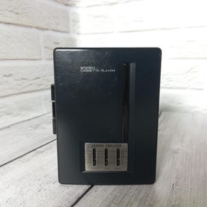 May include: A black Sharp stereo cassette player featuring a vertical design with a built-in graphic equaliser. The front panel displays the text Sharp Stereo Cassette Player and Graphic Equaliser, with three vertical sliders for audio adjustment.