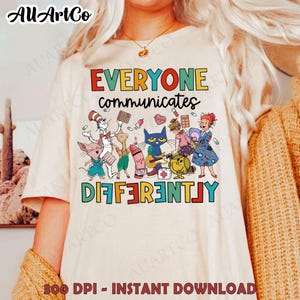 Puede incluir: Una camiseta blanca con un gráfico colorido que presenta personajes de libros infantiles populares. El texto "Everyone communicates differently" está impreso en colores arcoíris.