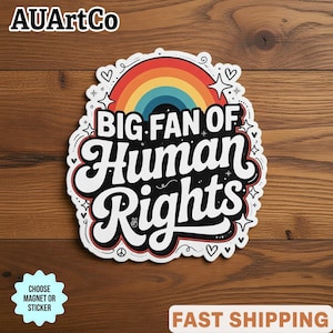 May include: A sticker with the text "BIG FAN OF Human Rights" in a bold, retro font, featuring a rainbow and decorative elements. The sticker has a white border and is set against a wooden background.