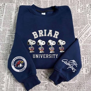 May include: Navy blue Briar University sweatshirt featuring Snoopy characters in football jerseys. The sweatshirt has the words "Briar University" across the chest and "Off Campus" on the sleeve. A Briar University Hawks logo is on the other sleeve.