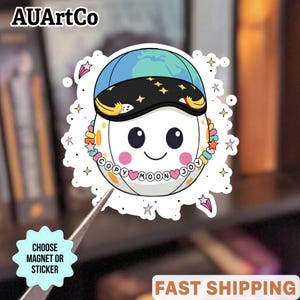 Pode incluir: Um adesivo branco com um personagem de lua de desenho animado usando um boné azul e preto com um design de globo. A lua tem um rosto sorridente, bochechas rosadas e um colar com as palavras "COPY MOON JOY". O adesivo tem um design de estrela e ponto.