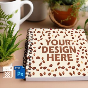 Könnte beinhalten: Spiralgebundenes Notizbuch mit beigem Einband, übersät mit Kaffeebohnen-Illustrationen. Der Text "YOUR DESIGN HERE" ist prominent dargestellt. Eine weiße Kaffeetasse mit Farnmuster und kleine Topfpflanzen befinden sich im Hintergrund.