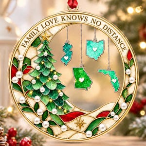 May include: A circular acrylic ornament featuring a gold frame with the text FAMILY LOVE KNOWS NO DISTANCE. The design includes a green Christmas tree, white pearls, and four hanging state map cutouts with white hearts, suspended by a red ribbon.