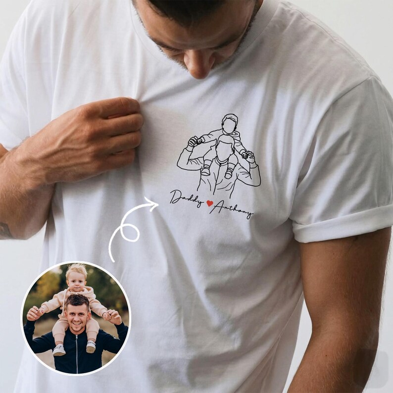 May include: White t-shirt featuring a line drawing of a person carrying a child on their shoulders. The text "Daddy ❤️ Anthony" is below the drawing. A photo of a person with a child on their shoulders is in a circle.