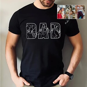 Peut inclure: T-shirt noir avec le mot "DAD" en blanc, chaque lettre repr&eacute;sentant une illustration familiale diff&eacute;rente. Le t-shirt comprend un petit collage de photos de famille. Un homme porte le t-shirt.