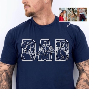 Peut inclure: T-shirt bleu marine avec le mot "DAD" en lettres blanches. Chaque lettre pr&eacute;sente un dessin au trait d'un p&egrave;re avec un enfant. Le t-shirt comporte &eacute;galement une petite image de trois photos de p&egrave;res et d'enfants.