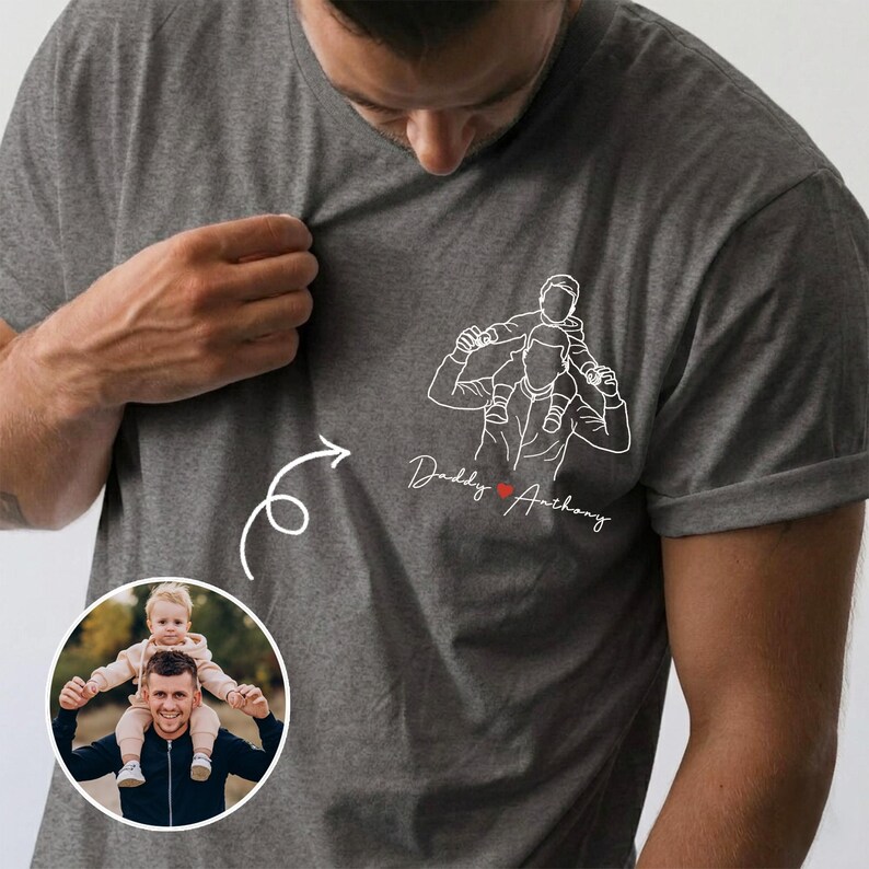 May include: Gray t-shirt featuring a white line drawing of a person carrying a child on their shoulders. The text "Daddy Anthony" is below the drawing, with a red heart. A circular photo shows a person with a child on their shoulders.