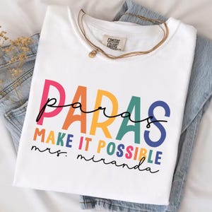 May include: White t-shirt with the text "paras make it possible mrs. miranda" in rainbow colors.