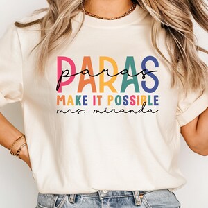 May include: A white t-shirt with the text "paras make it possible mrs. miranda" in rainbow colors.