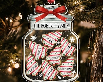 May include: A clear, jar-shaped Christmas ornament with a red ribbon and the year 2025. Inside, tree-shaped cookies are decorated with red and white stripes, each bearing a name. The text "THE ROBERT FAMILY" is displayed on the jar.