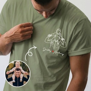 May include: Olive green t-shirt featuring a line drawing of a person carrying a child on their shoulders, with the text "Daddy Anthony" and a heart. A circular photo of a person with a child is in the lower left corner.