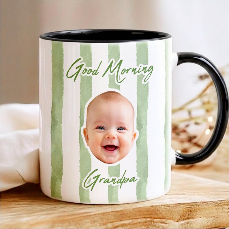 May include: A white ceramic mug with a black handle and interior, featuring vertical sage green watercolor stripes. The mug displays the text Good Morning and Grandpa in green script, with a centered photographic portrait of a smiling baby.