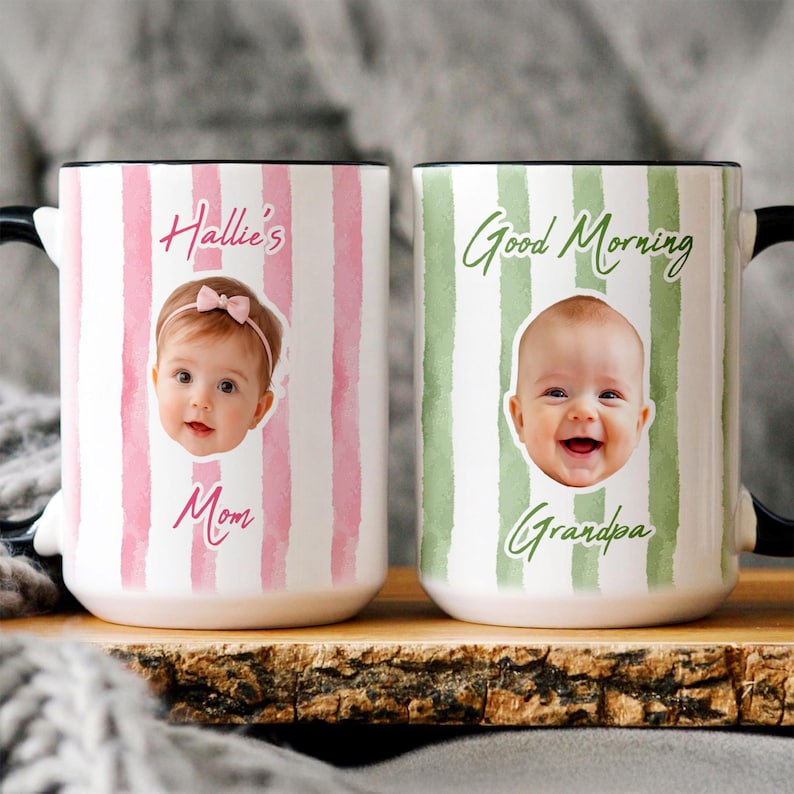 May include: Two ceramic mugs with black handles. The left mug has pink vertical stripes, a photo of a baby with a pink bow, and the text Hallie's Mom. The right mug has green vertical stripes, a photo of a baby, and the text Good Morning Grandpa.