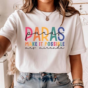 May include: White t-shirt with a rainbow colored graphic that says "paras make it possible mrs. miranda".