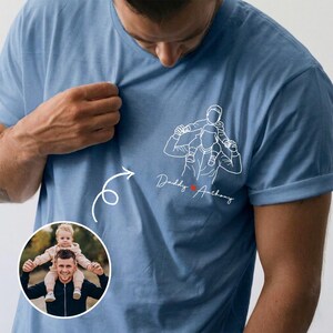 May include: Light blue t-shirt featuring a white line drawing of a father carrying a child on his shoulders, with the text "Daddy Anthony" and a heart. A circular photo of a father and child is in the lower left.