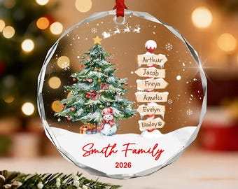 May include: A round, faceted glass Christmas ornament with a red ribbon hanger. The design features a decorated Christmas tree, a snowman, and a signpost with the names Arthur, Jacob, Freya, Amelia, Evelyn, and Bailey. Text reads Smith Family 2026.