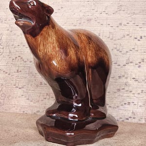 May include: A brown ceramic bear figurine with a glossy finish. The bear is standing on its hind legs with its mouth open. The figurine has a detailed fur texture and is a decorative item.