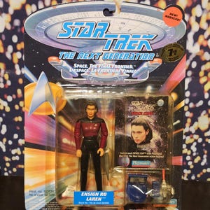 May include: A Star Trek: The Next Generation action figure of Ensign Ro Laren in a sealed package. The figure is wearing a red and black uniform. The packaging includes the show's logo and the text "SPACE. THE FINAL FRONTIER".