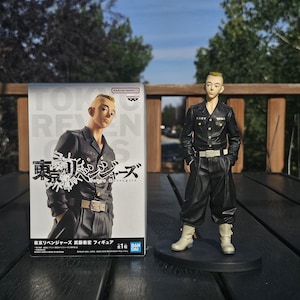 Könnte beinhalten: Figur einer Figur aus "Tokyo Revengers" in schwarzer Uniform mit weißen Stiefeln, die auf einer schwarzen Basis steht. Die Figur befindet sich neben ihrer Box mit japanischem Text und einem Bild der Figur.